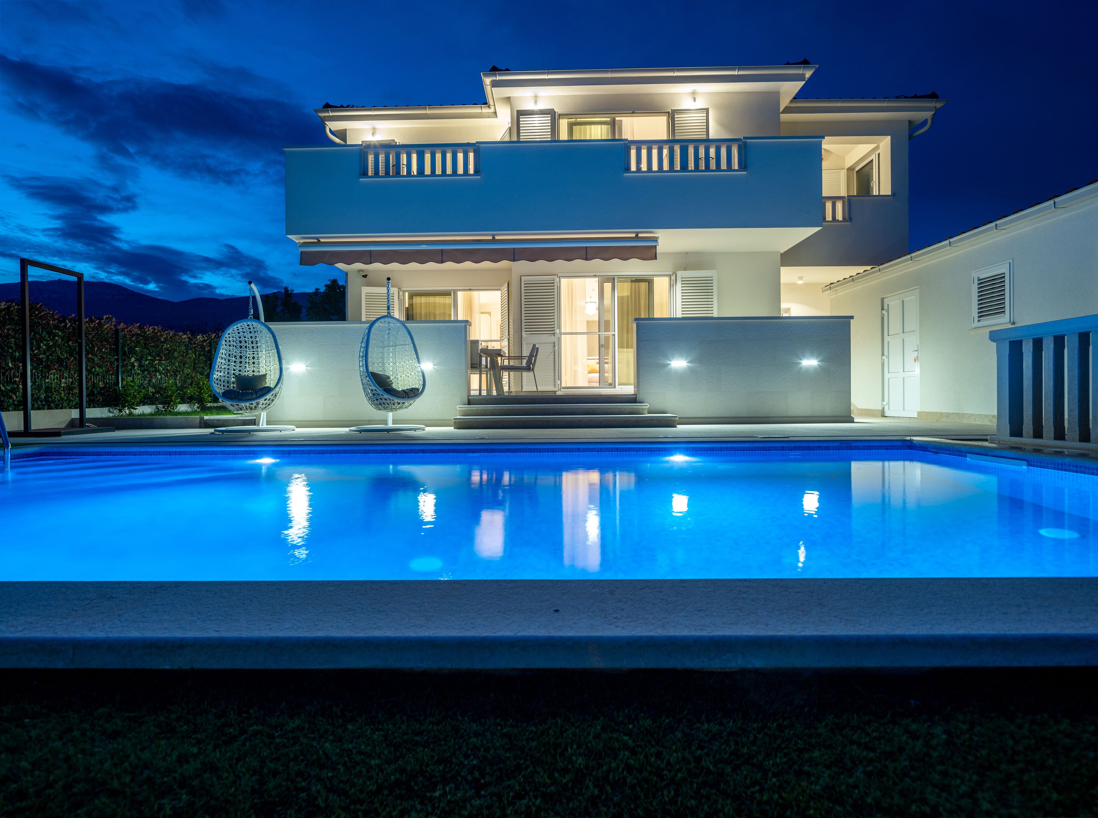 A modern two-story house with a swimming pool, a covered patio, and hanging chairs.