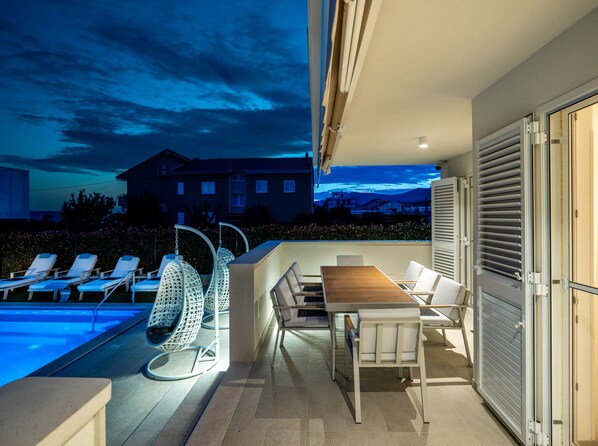 Eine Dachterrasse mit Pool, Liegestühlen, einem Tisch und Blick auf ein Gebäude im Hintergrund.