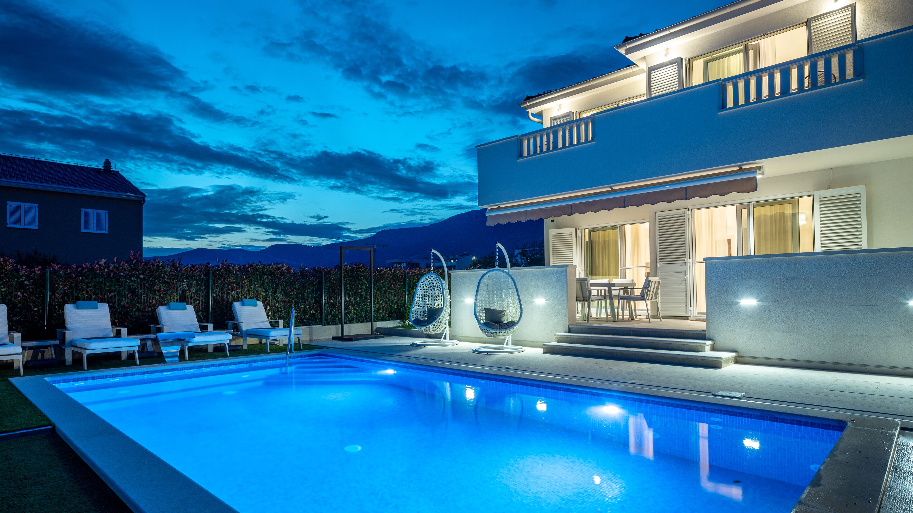 A modern poolside area with a swimming pool, lounge chairs, and a dining set.