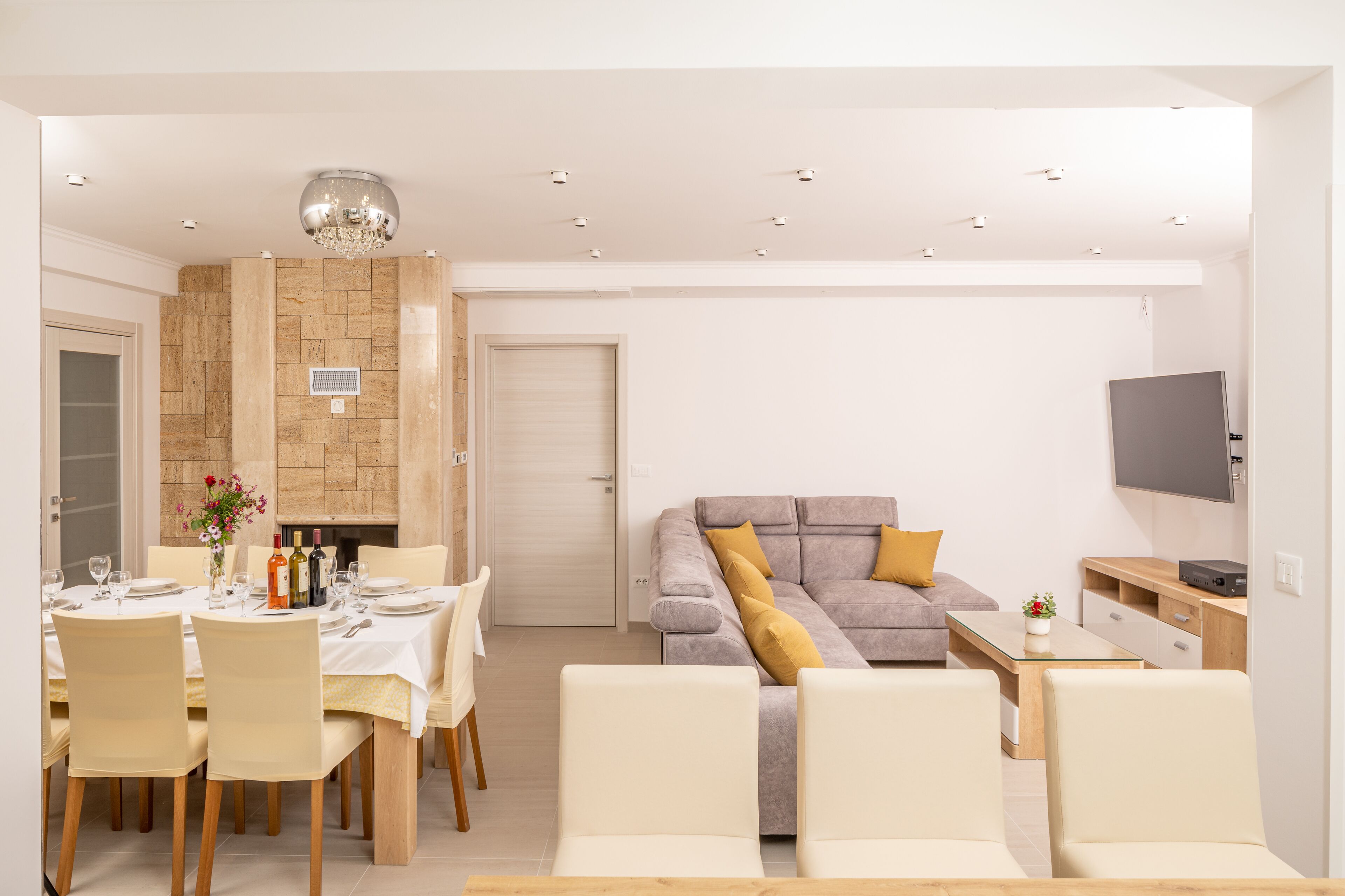 A modern living room with a sofa, a dining table set for four, and a television mounted on the wall.