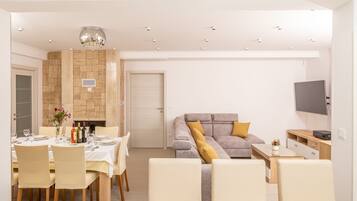 A modern living room with a sofa, a dining table set for four, and a television mounted on the wall.