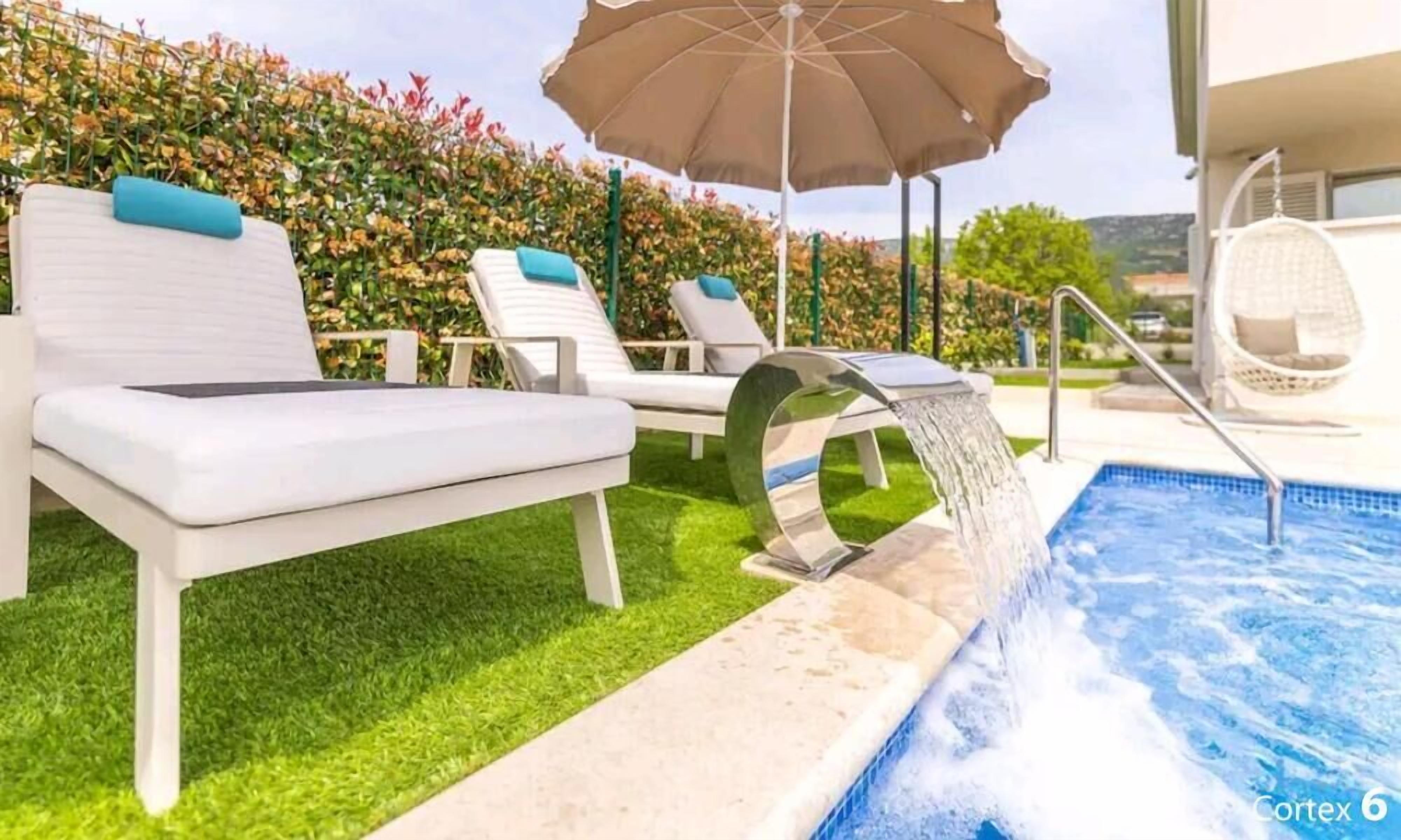 A poolside area with lounge chairs, a water feature, and a garden backdrop.