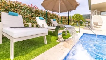 A poolside area with lounge chairs, a water feature, and a garden backdrop.