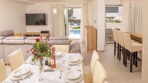 A dining area with a table set for four, a sofa, a TV, and a view of an outdoor pool. - Luxury villa Bachin - family villa (Kastela)