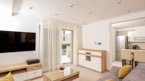 A modern living room with a flat-screen TV, a glass coffee table, a sofa, and a kitchen area with a refrigerator and microwave. - Luxury villa Bachin - family villa (Kastela)