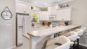 A modern kitchen with white cabinetry, a central island with bar seating, a microwave, and a refrigerator. - Kings Hideaway - Near DT! (Branson)