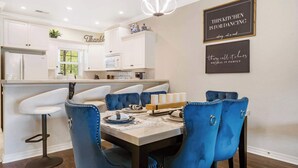 A modern kitchen with white cabinets, a dining area with blue upholstered chairs, and two framed quotes on the wall. - Kings Hideaway - Near DT! (Branson)
