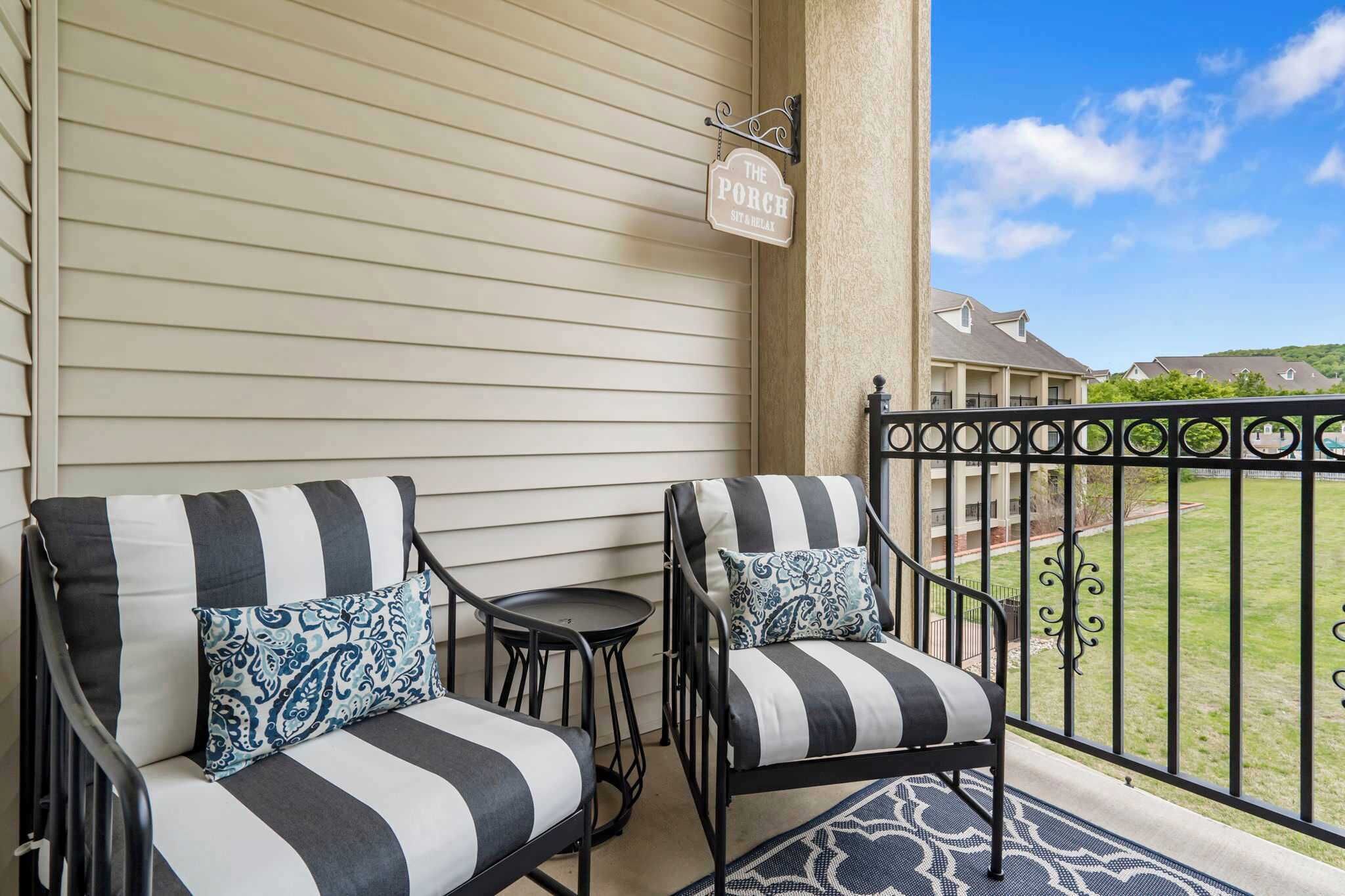 A balcony with two black and white striped sofas, a small round table, and a decorative sign reading "The Porch."