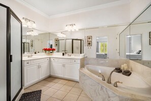A modern bathroom with a large mirror, two sinks, a bathtub, and a vanity with cabinets.