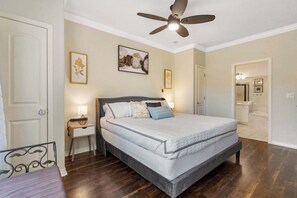 A bedroom with a bed, bedside tables, a ceiling fan, and artwork on the walls.