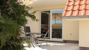 A patio area with a chair and a table, a sliding glass door leading to an interior space, and a tiled roof. - Apartment "Meine Auszeit", 2 adults + 1 infant, 1 bathroom, terrace, WLAN (Koserow)
