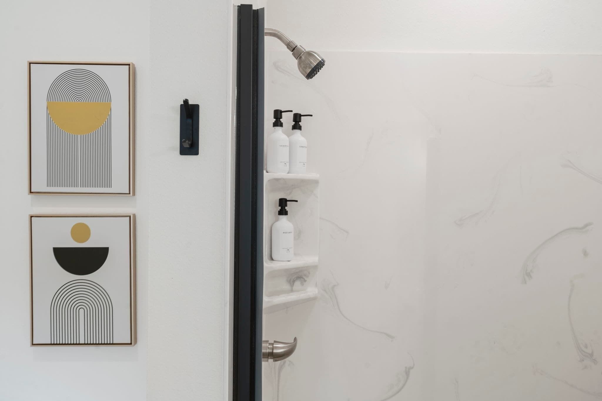 A bathroom with a shower, a framed abstract artwork, and a shelf with toiletries.