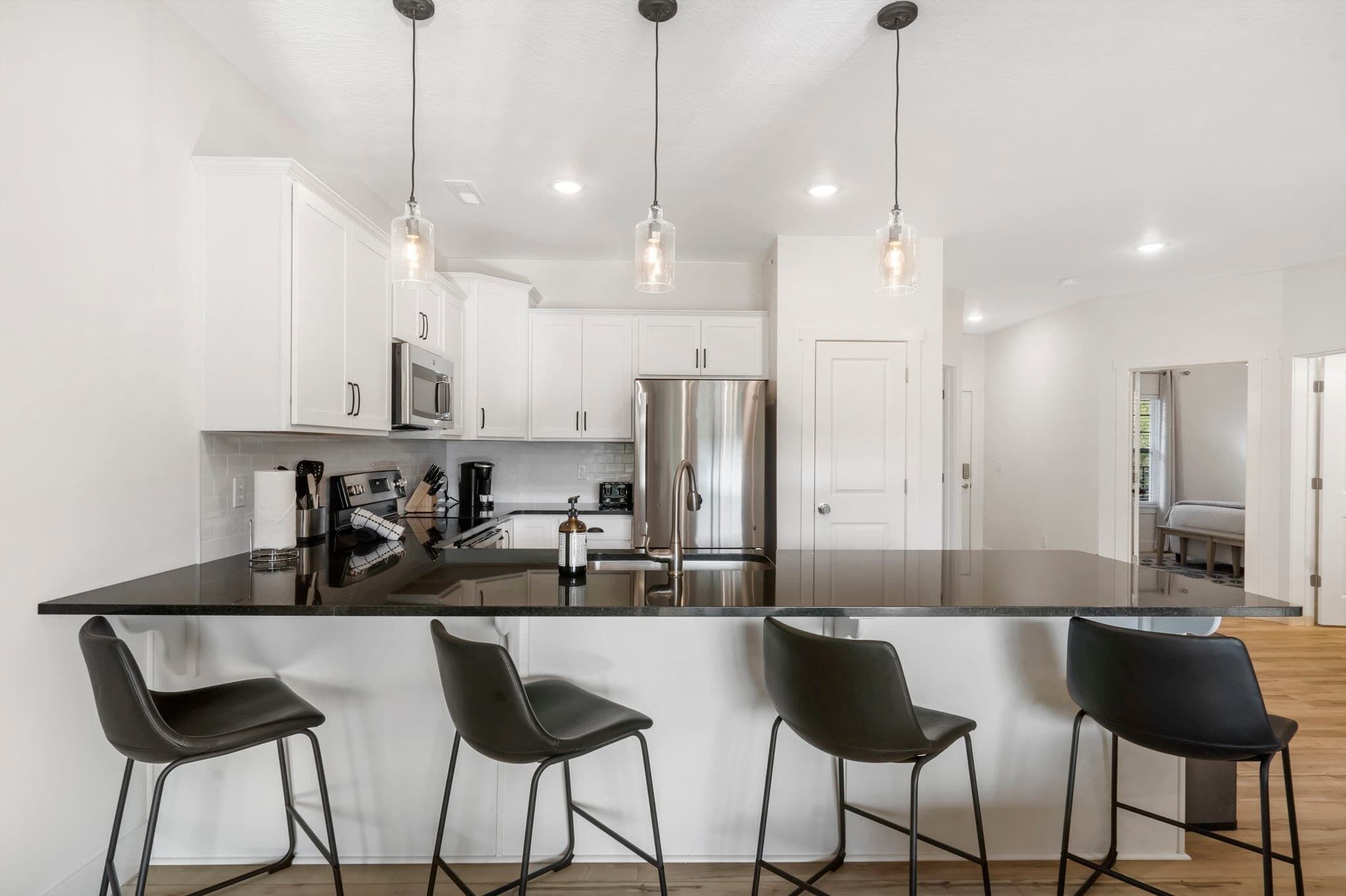 A modern kitchen with white cabinets, stainless steel appliances, and black bar stools.