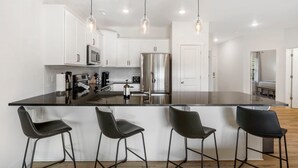 A modern kitchen with white cabinets, stainless steel appliances, and black bar stools. - New Lakeview Penthouse - Amenities Galore! (Branson)