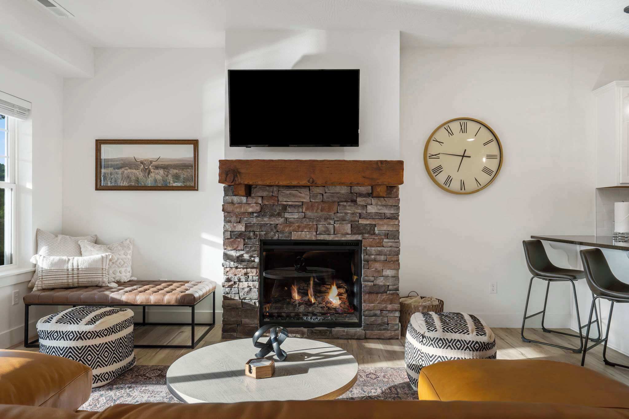 A living room with a stone fireplace, a mounted TV, and a wall clock.