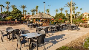 An outdoor patio area with tables and chairs, surrounded by palm trees and a thatched-roof structure. - Laura's Villa at Regal Palms (Davenport)