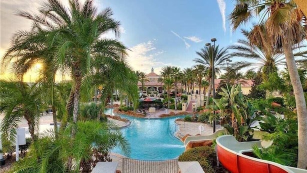 A resort with a central swimming pool, palm trees, and a building in the background. - Laura's Villa at Regal Palms (Davenport)