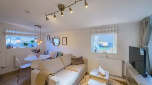 A modern living room with a white sofa, a dining table, and a TV on a stand. - Prinshöjden Hotel - Apartments & Villas (Katrineholm)