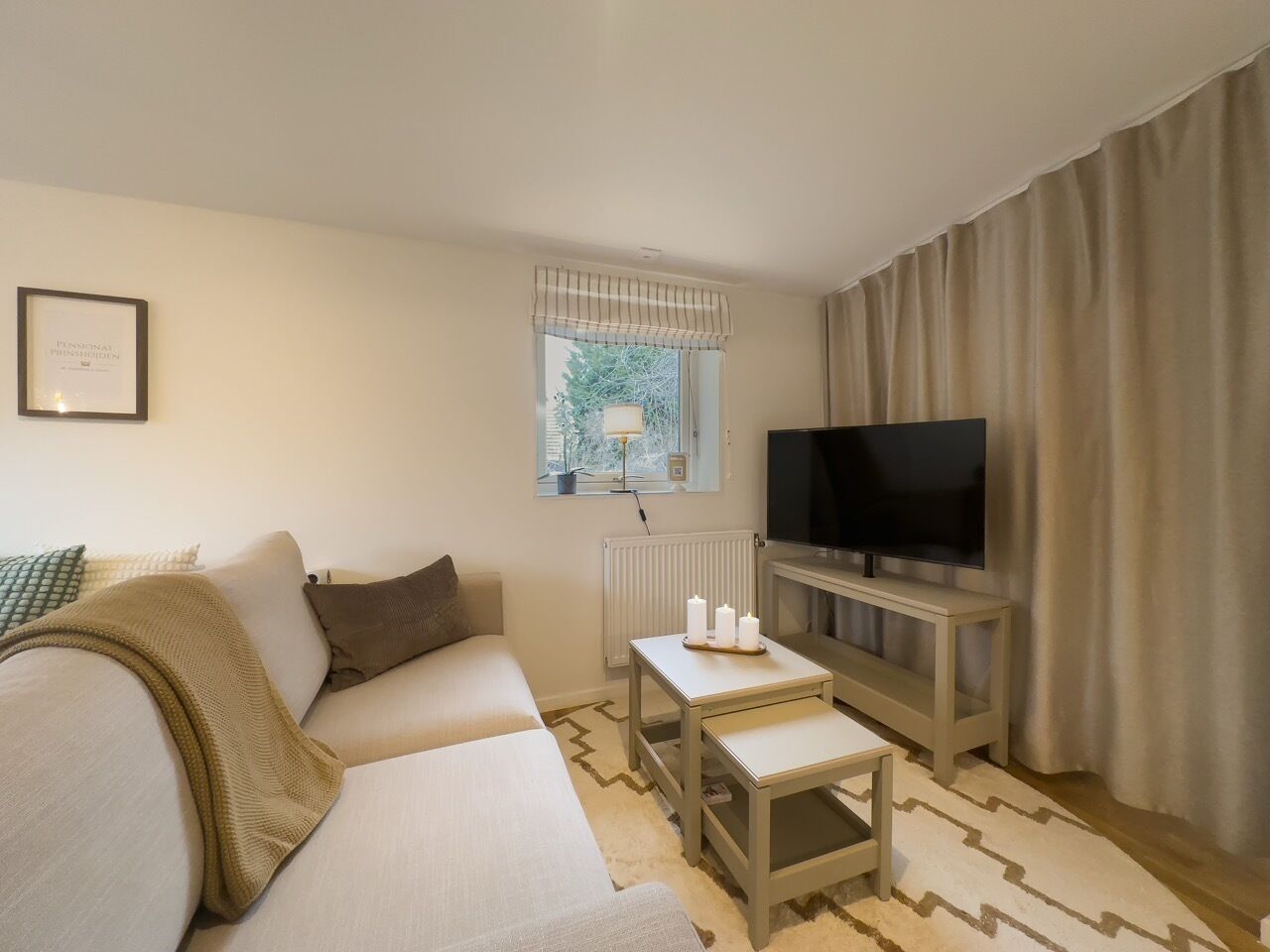 Een hotelkamer met een bank, een klein tafeltje met kaarsen, een televisie op een standaard en een raam met gordijnen.