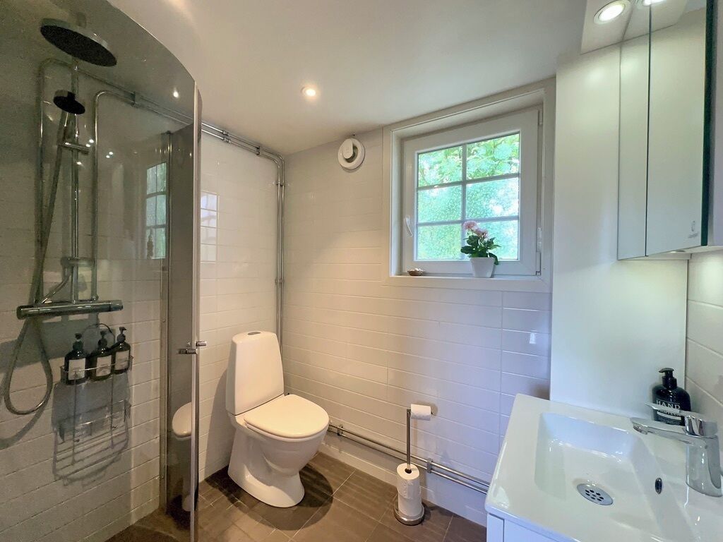 Ein Badezimmer mit Duschkabine, Toilette, Waschbecken und einem Fenster mit einer Pflanze.