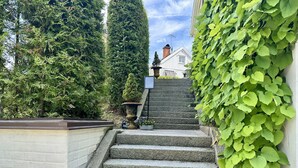 A stone staircase leading to a white building with a chimney, surrounded by lush greenery and a small garden with a decorative urn. - Prinshöjden Hotel - Apartments & Villas (Katrineholm)