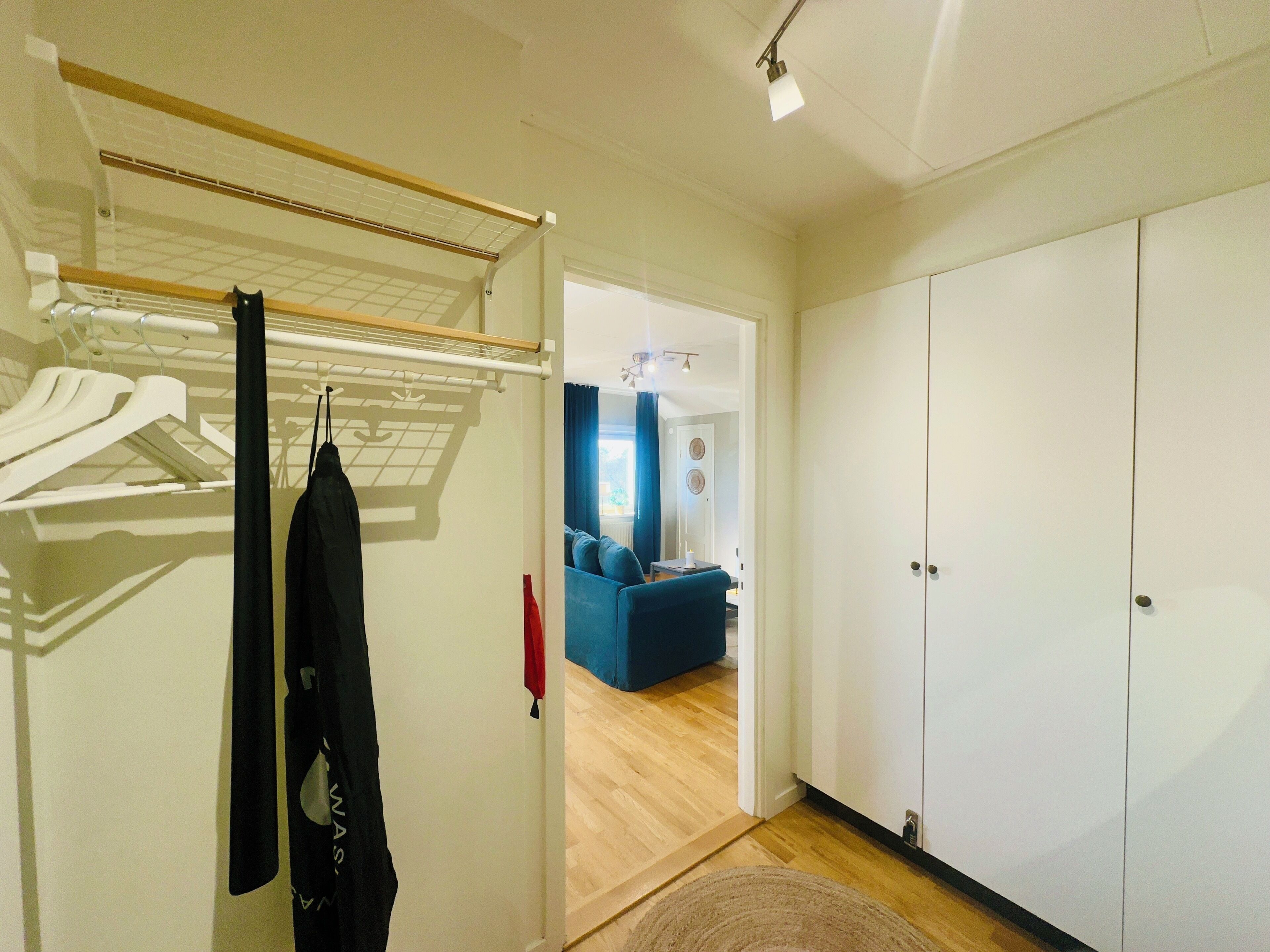 Una habitación con armario, tendedero y una vista parcial de una sala de estar con un sofá azul.
