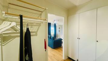 Una habitación con armario, tendedero y una vista parcial de una sala de estar con un sofá azul.