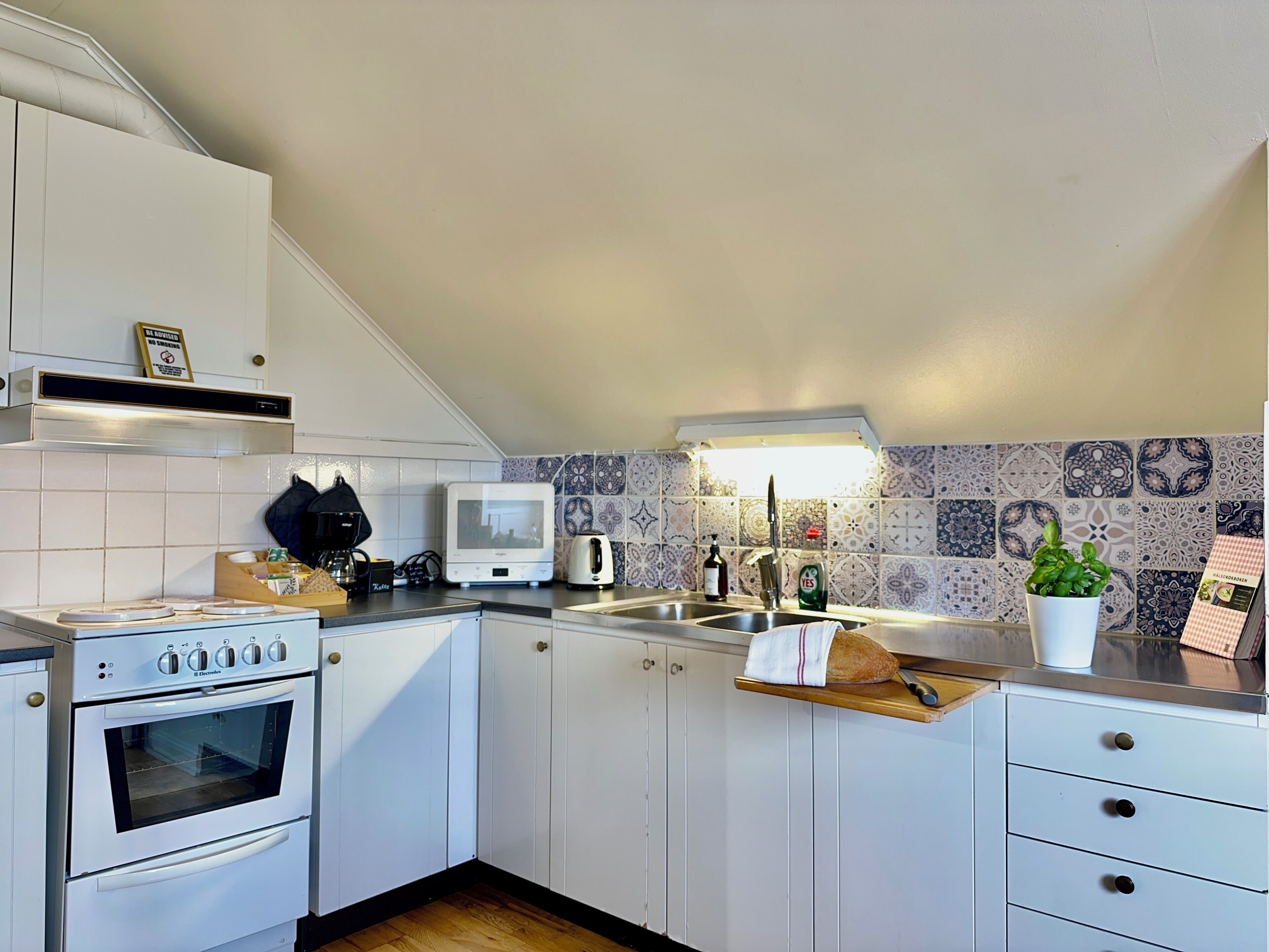 Una cocina con armarios blancos, horno empotrado, cafetera, hervidor y un lavabo con salpicadero de azulejos.