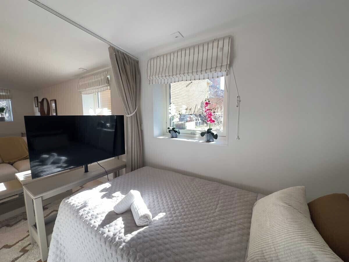 Habitación de hotel con cama, televisor en un mueble bajo, ventana con cortinas y vistas al exterior.