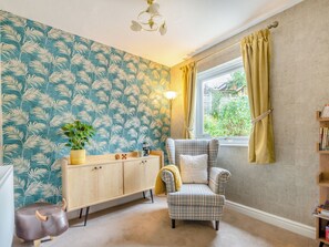 Una habitación acogedora con un sillón de cuadros, un aparador de madera y un pequeño taburete con forma de toro.