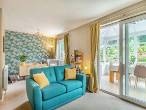 Una sala de estar moderna con un sofá color turquesa, una zona de comedor con una mesa y sillas, y un amplio ventanal corredero que da a un jardín.