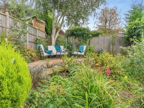 A garden with a wooden fence, two chairs, and a table with a blanket and wine glasses. - 2 bedroom accommodation in Ashbourne (Ashbourne)