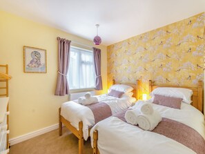 Un dormitorio con dos camas, una ventana con cortinas, una pared con un diseño de pájaros, un cuadro enmarcado y una lámpara de noche.