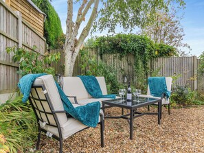 An outdoor seating area with a glass table and two chairs, surrounded by a wooden fence and greenery.