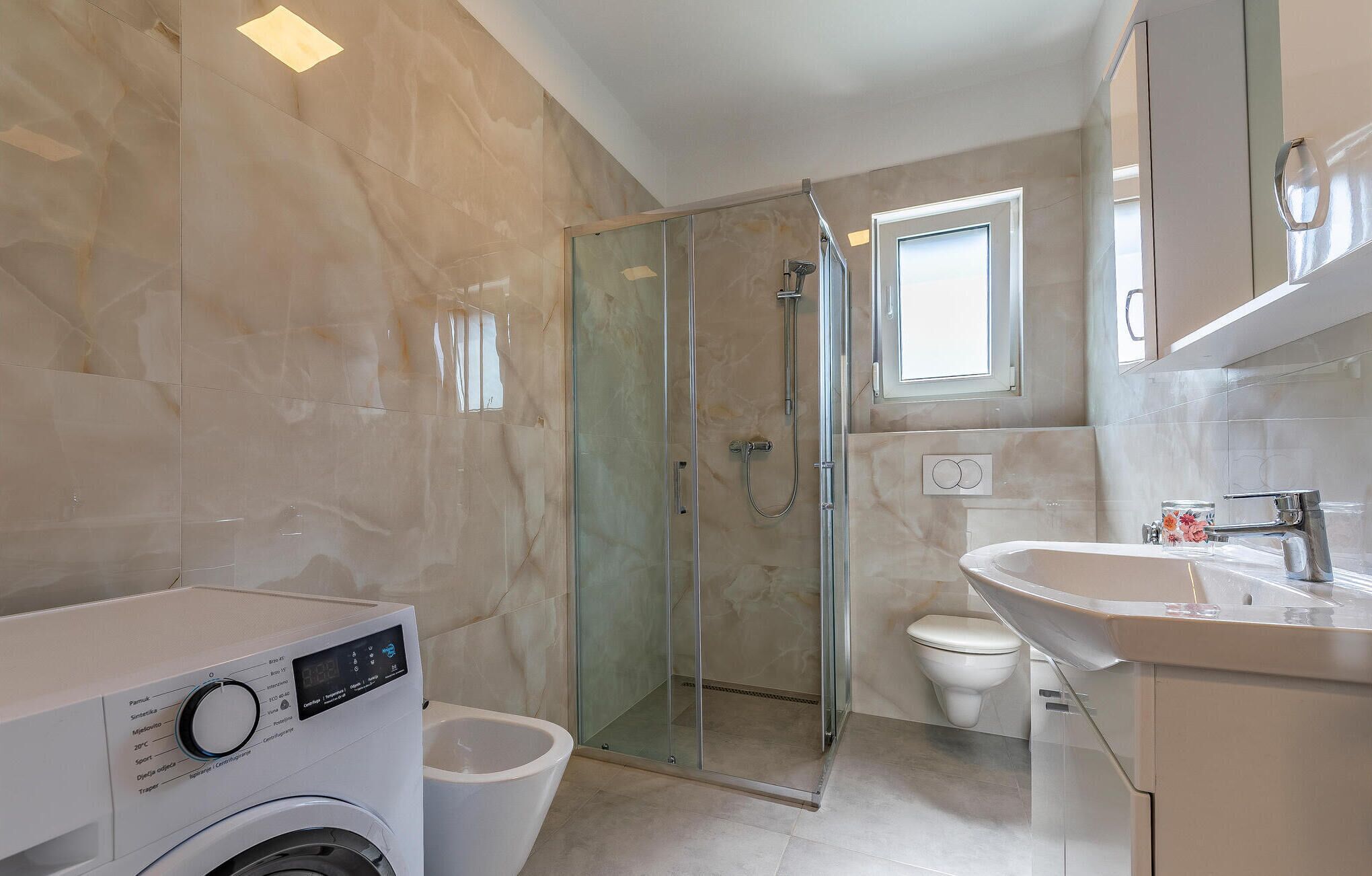 A modern bathroom with a glass-enclosed shower, a toilet, and a washing machine.