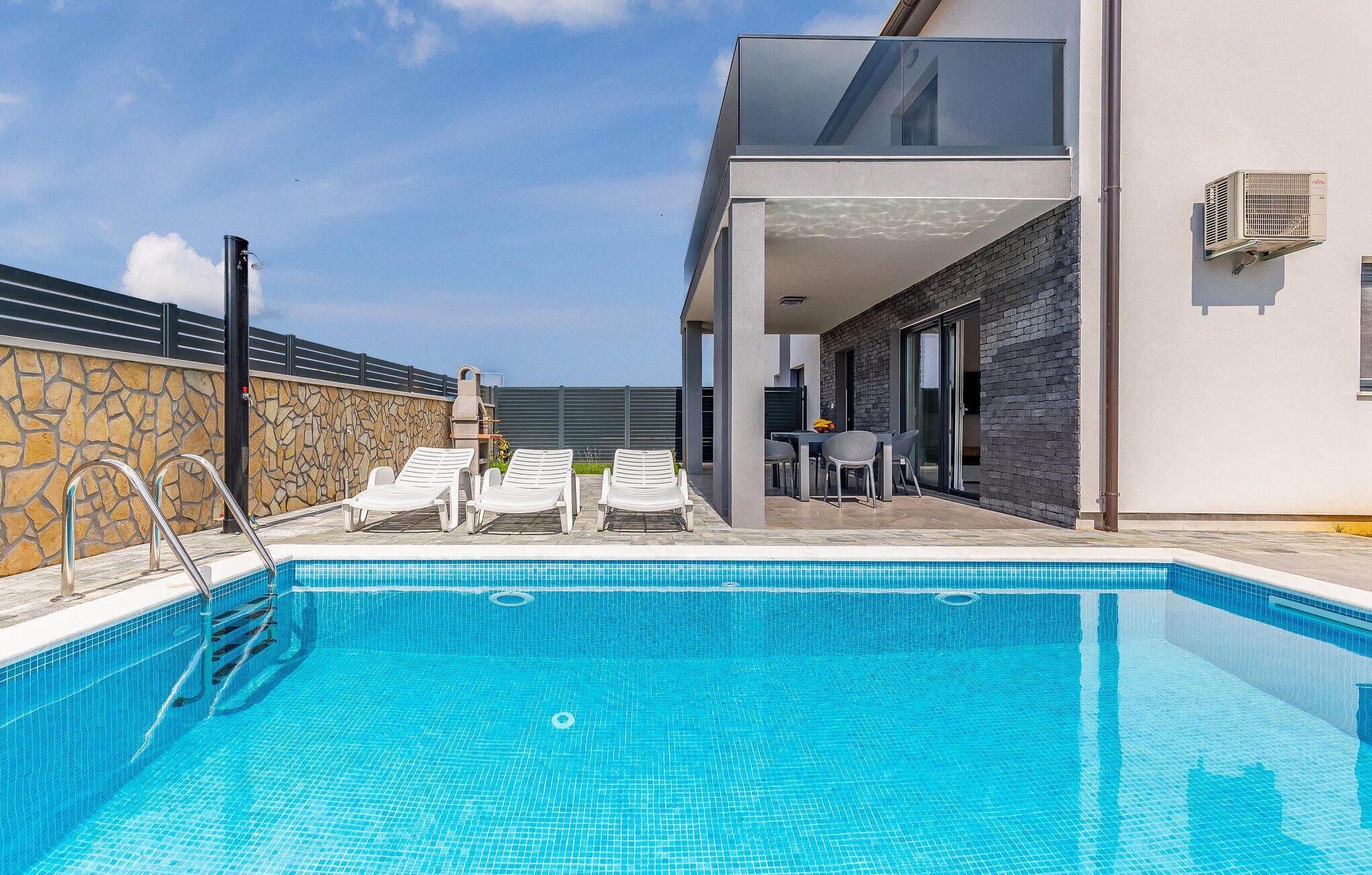 Ein moderner Poolbereich mit klarem, blauem Pool, Liegestühlen und einer Terrasse mit Tisch und Stühlen.