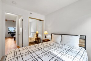 A bedroom with a bed, two bedside tables with lamps, a mirror, and a door leading to another room. - Mile High Mountain - Carson Valley Views (Stateline)