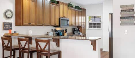 A modern kitchen with wooden cabinets, a central island with bar stools, a microwave, and a coffee maker.