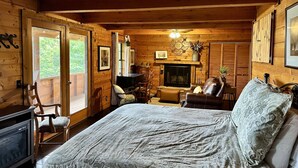 Acogedora habitación tipo cabaña de madera con cama, chimenea, mesa de comedor y un gran ventanal.