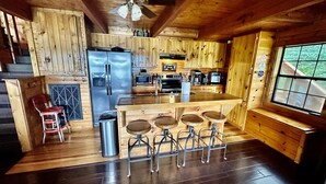 Interior de una cabaña de madera con cocina, barra y mesa de comedor.