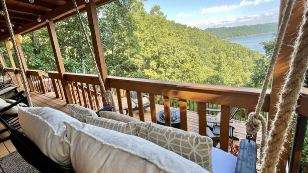 Una terraza de madera con mobiliario exterior, vistas a un lago y una ladera boscosa.