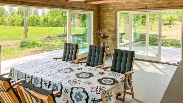 A covered outdoor dining area with a table and chairs, large windows, and a view of a green landscape. - Cozy home in Lammhult with sauna (Lammhult)