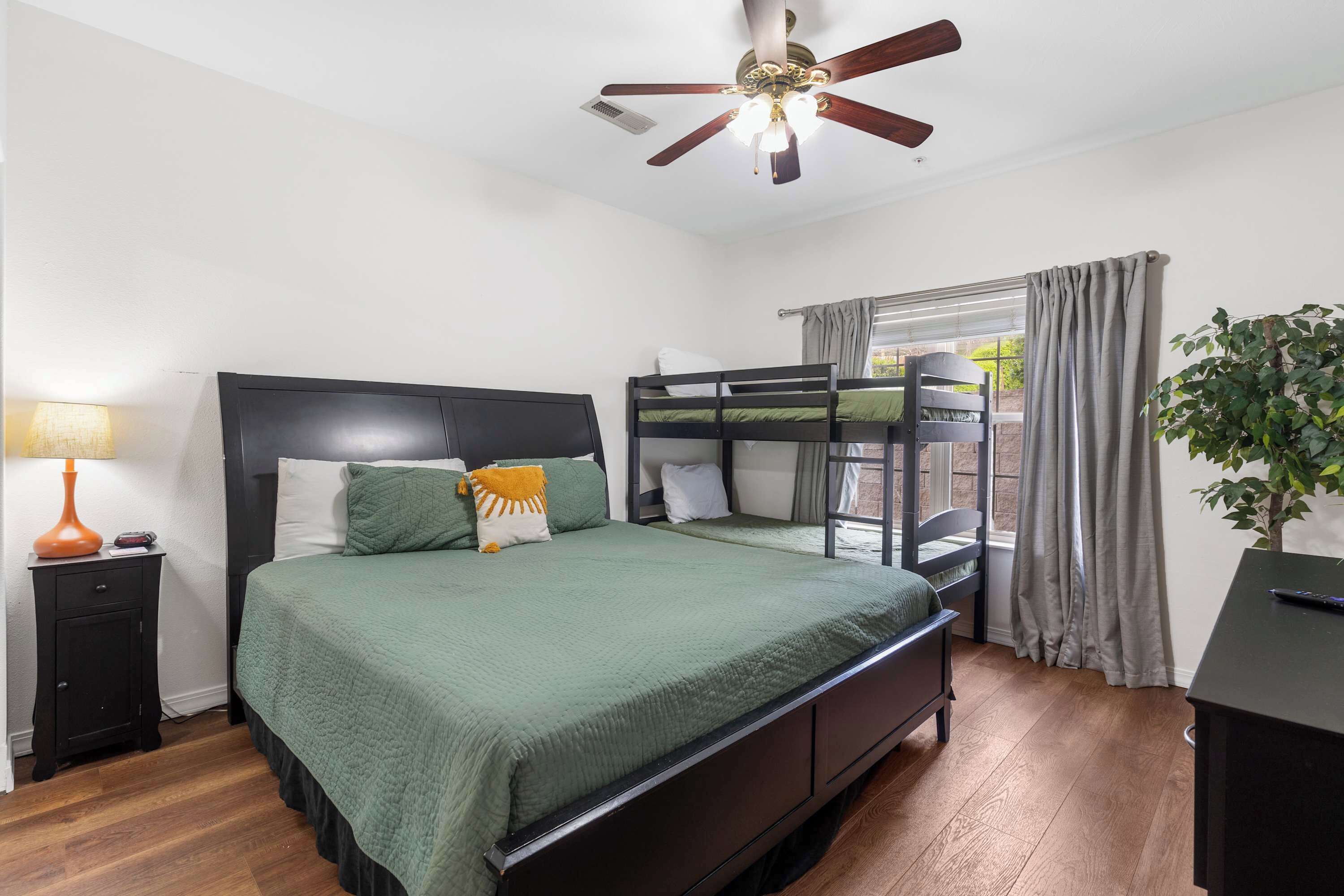 A bedroom with a bunk bed, a desk, a lamp, and a ceiling fan.