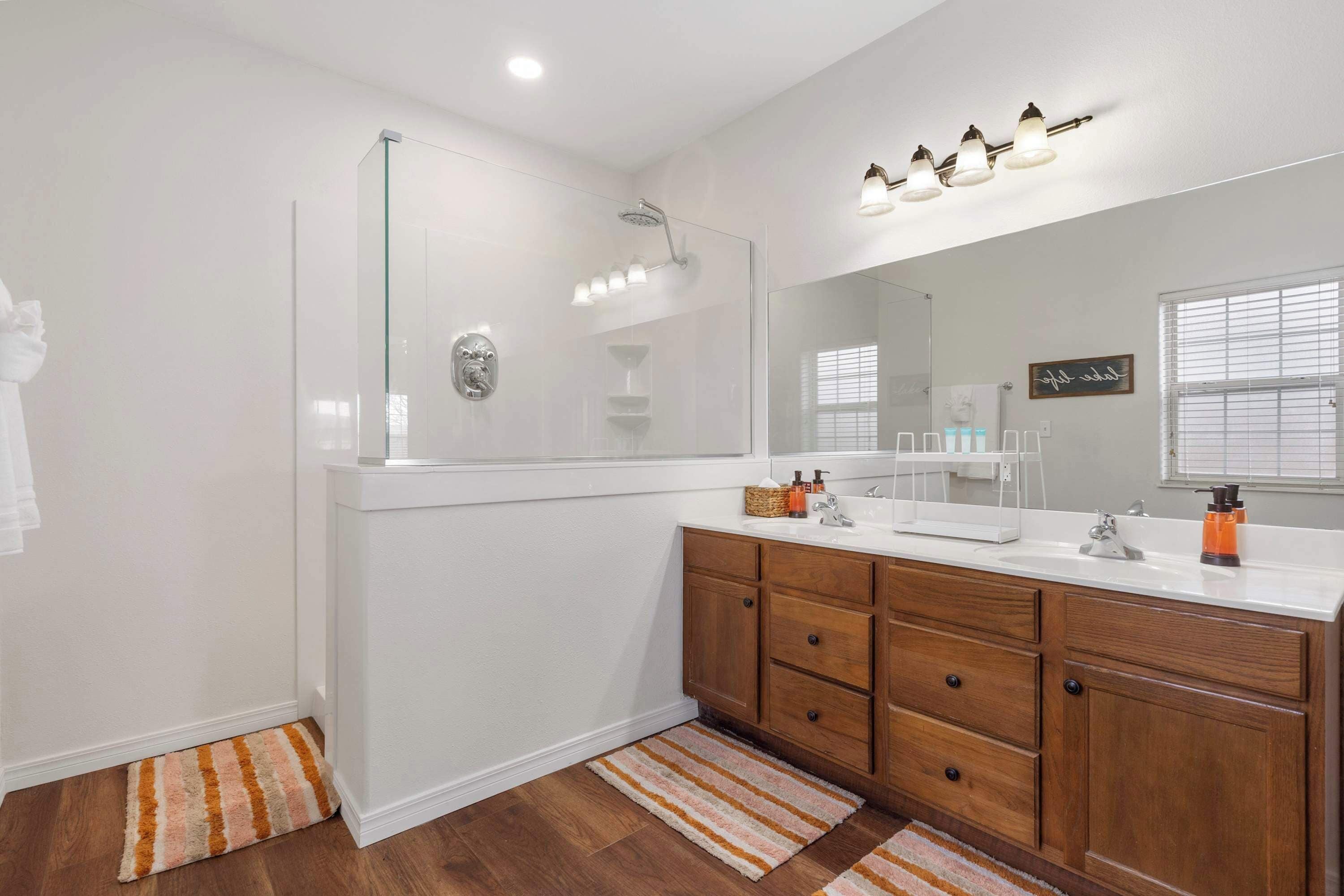 Un baño moderno con ducha de vidrio, armarios de madera y un espejo grande.