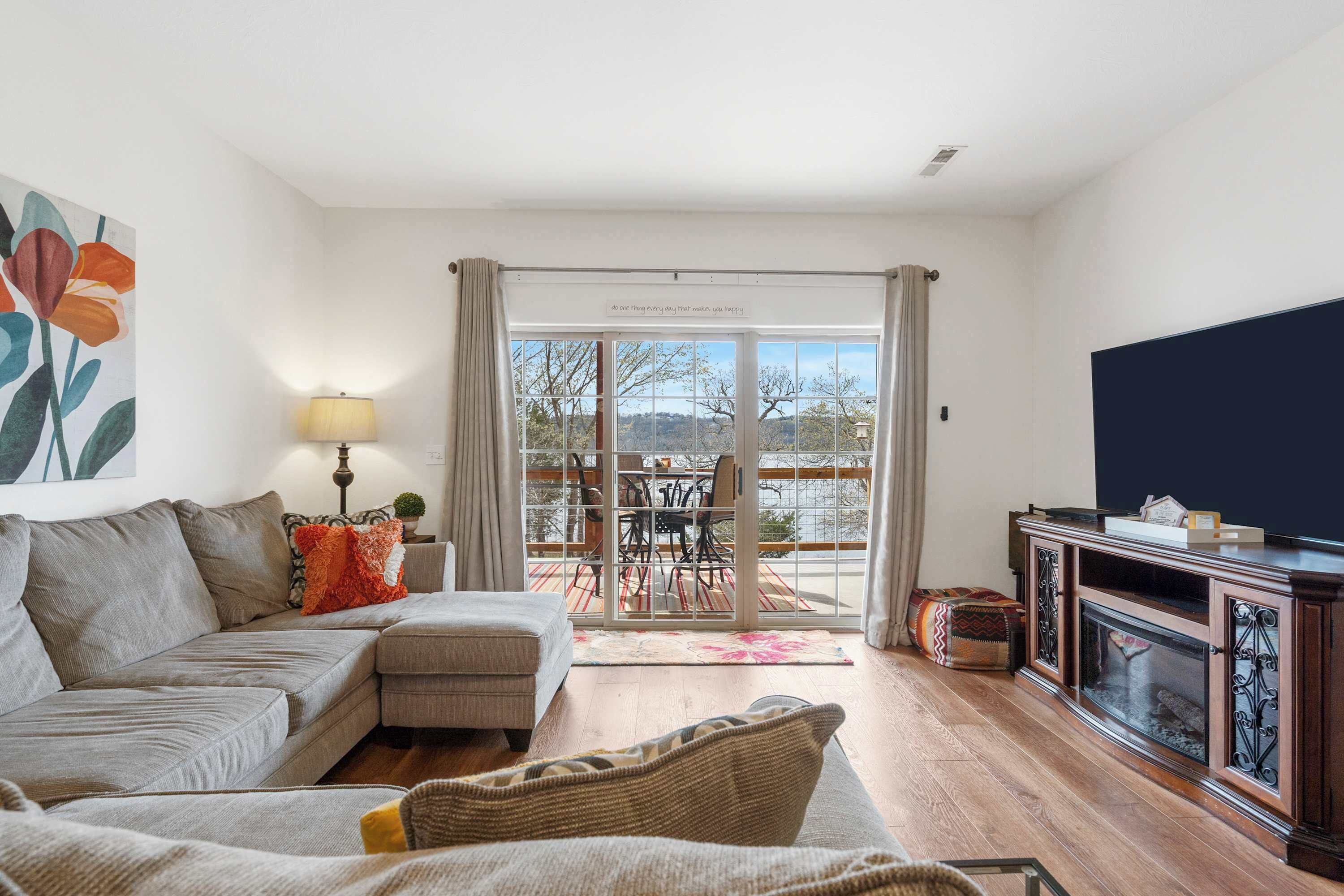 A living room with a sofa, armchair, and a fireplace. There is a television on the wall and a window with curtains.