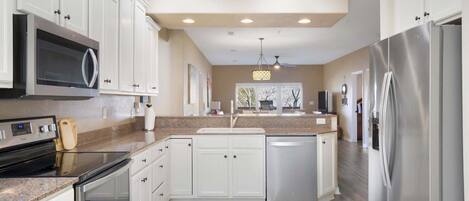 A modern kitchen with white cabinets, stainless steel appliances, granite countertops, and a central island.