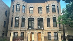 Um edifício de vários andares em tijolo com entrada na esquina, janelas amplas e grade de metal.
