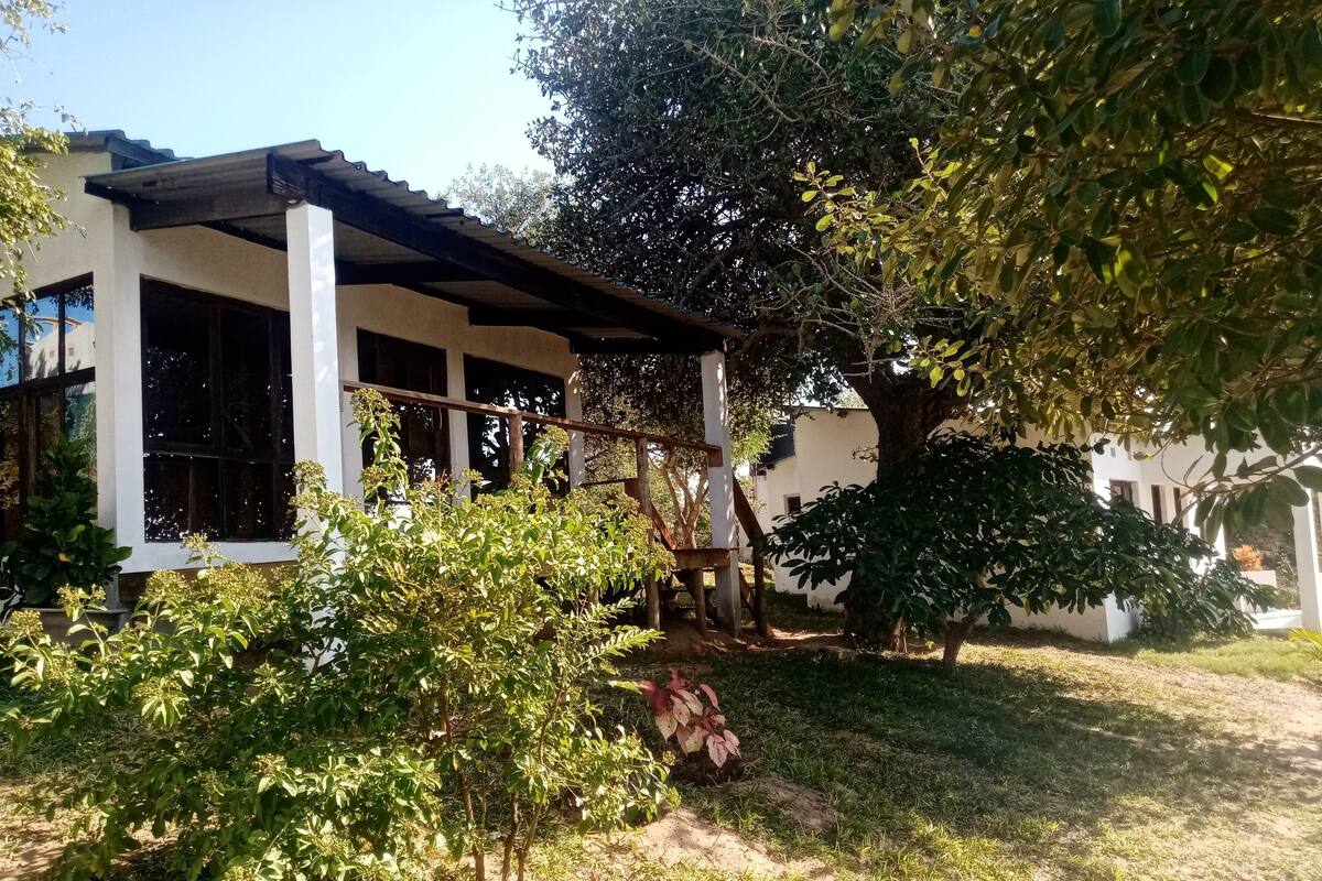 Ein Haus mit überdachter Veranda, einem kleinen Garten und einem Baum.
