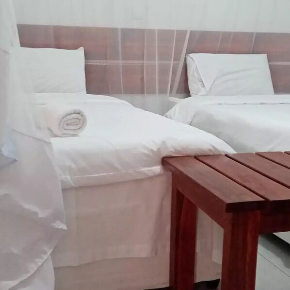 Ein Hotelzimmer mit zwei Betten, jeweils mit weißer Bettwäsche und Kissen, und einem Holztisch im Vordergrund.