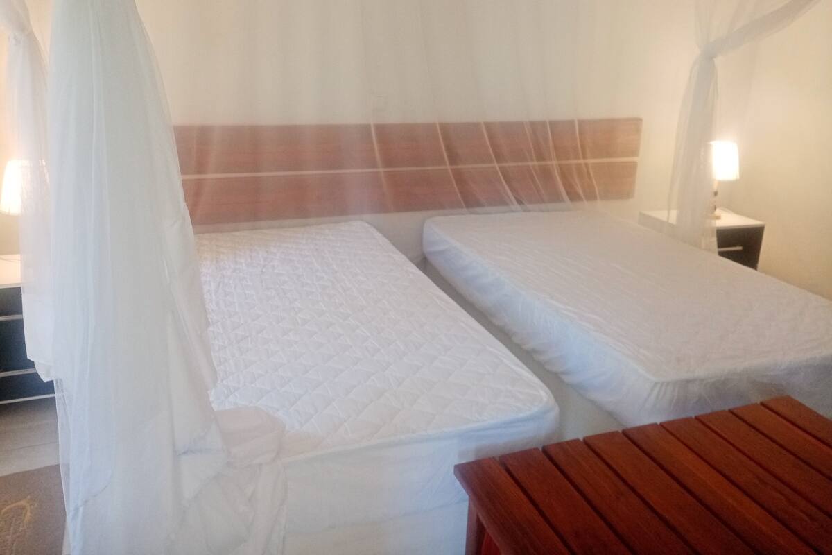 Ein Zimmer mit zwei Betten, einer Holzbank und einem Nachttisch mit Lampe.
